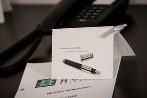 Een visitekaartje met een pen erop, bovenop een welkomstbrief, geplaatst op een bureau met een telefoon.