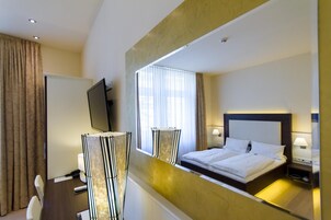 Hotelkamer met een groot bed, nachtkastjes, een televisie en een spiegel die de kamer weerspiegelt.