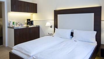 Een moderne hotelkamer met een groot bed, een kleine kitchenette en een nachtkastje met een lamp.