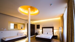 A modern hotel room with a large bed, a smaller bed, a standing fan, and a unique ceiling light fixture. - The Heidelberg Exzellenz Hotel (Heidelberg)