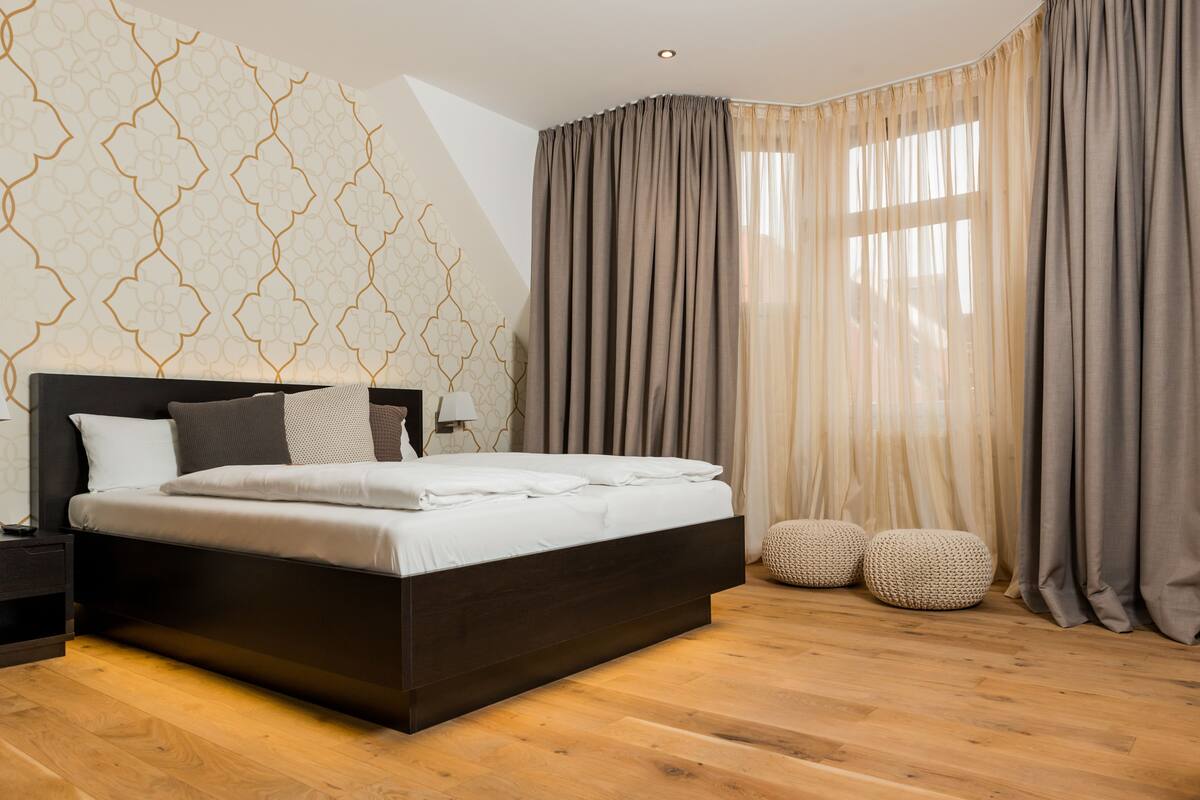 A modern bedroom with a dark wooden bed, a patterned wall, and sheer curtains.
