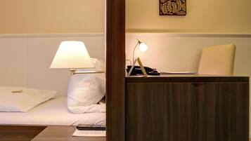 A hotel room with a bed, a bedside lamp, a desk with a lamp, and a telephone.