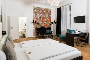Habitación de hotel con cama, sofá, escritorio, televisor y un tapiz colorido en la pared.