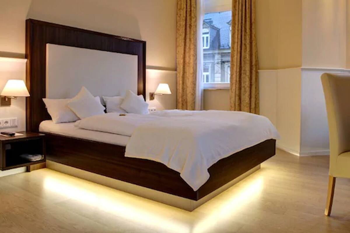 A modern hotel room with a large bed, two bedside tables, and a window with curtains.