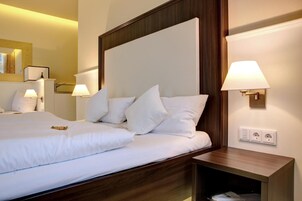 Una habitación de hotel con una cama grande, dos mesitas de noche con lámparas, un cabecero de madera y un enchufe en la pared.