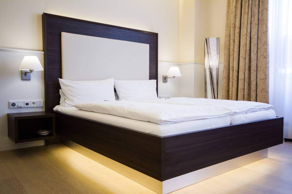 A modern hotel room with a large bed, bedside lamps, a nightstand, and a decorative wall piece.
