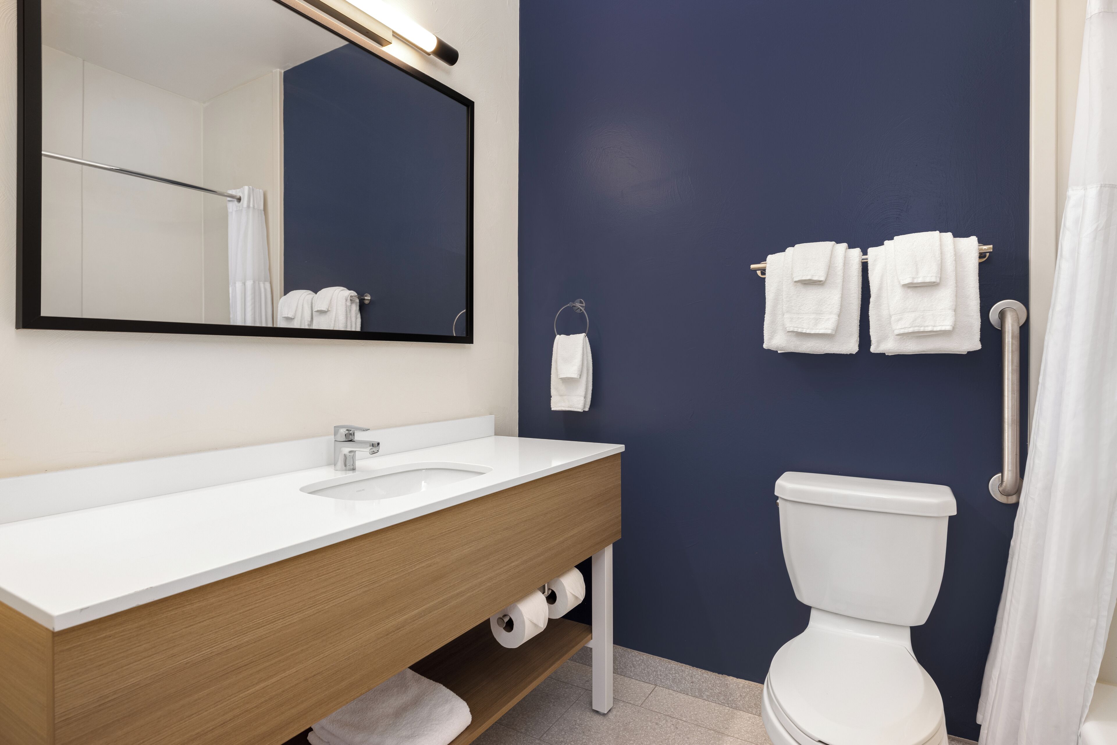 A bathroom with a white sink, mirror, and toilet, with towels hanging on a rack.