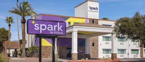 A hotel with a purple and yellow sign, palm trees, and a clear blue sky.