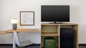 Une chambre d’hôtel équipée d’un bureau, d’une chaise, d’une télévision, d’une lampe, d’une œuvre d’art encadrée et d’une poubelle verte.
