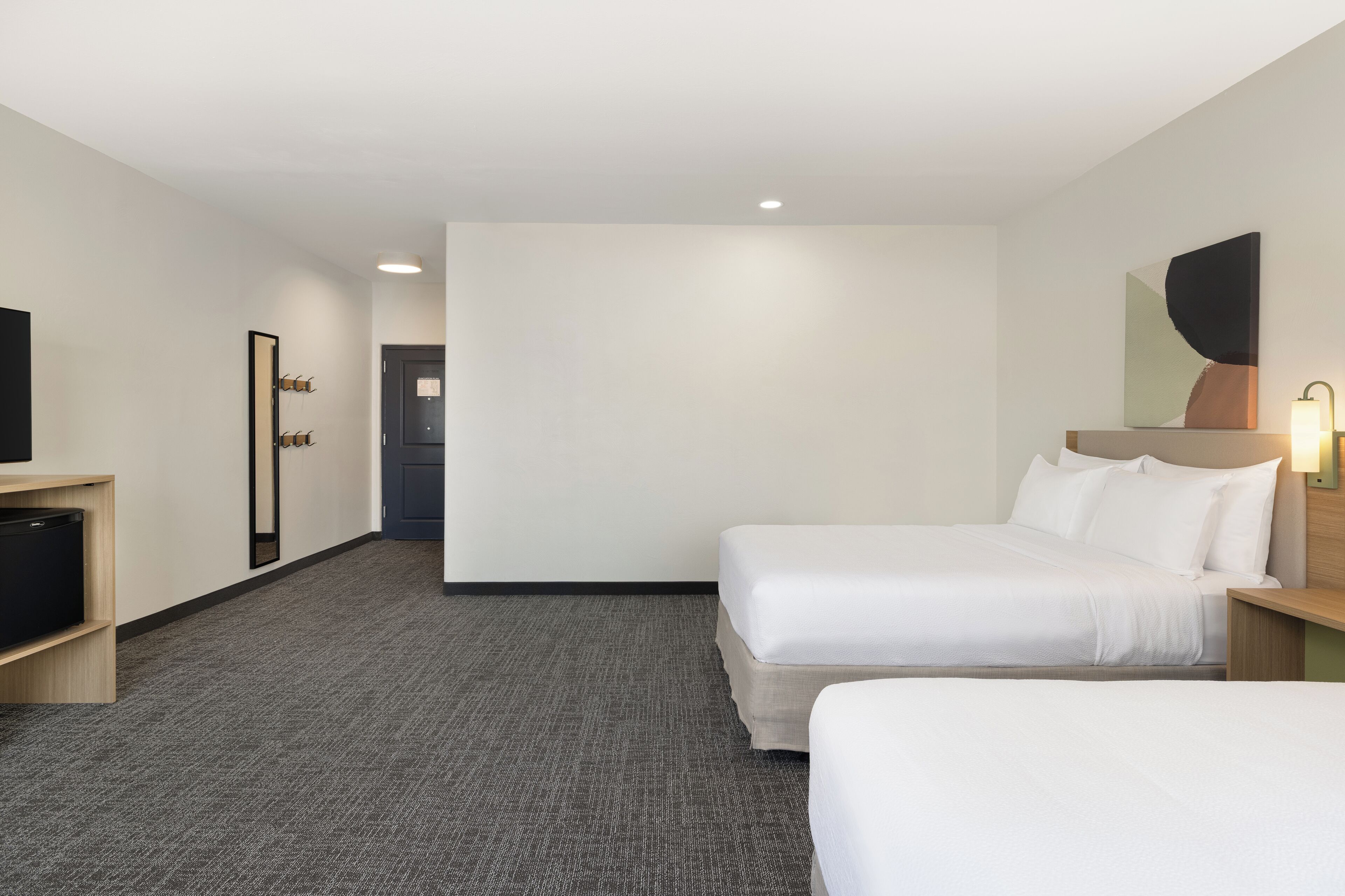 A hotel room with two beds, a TV, a desk, and a mirror.