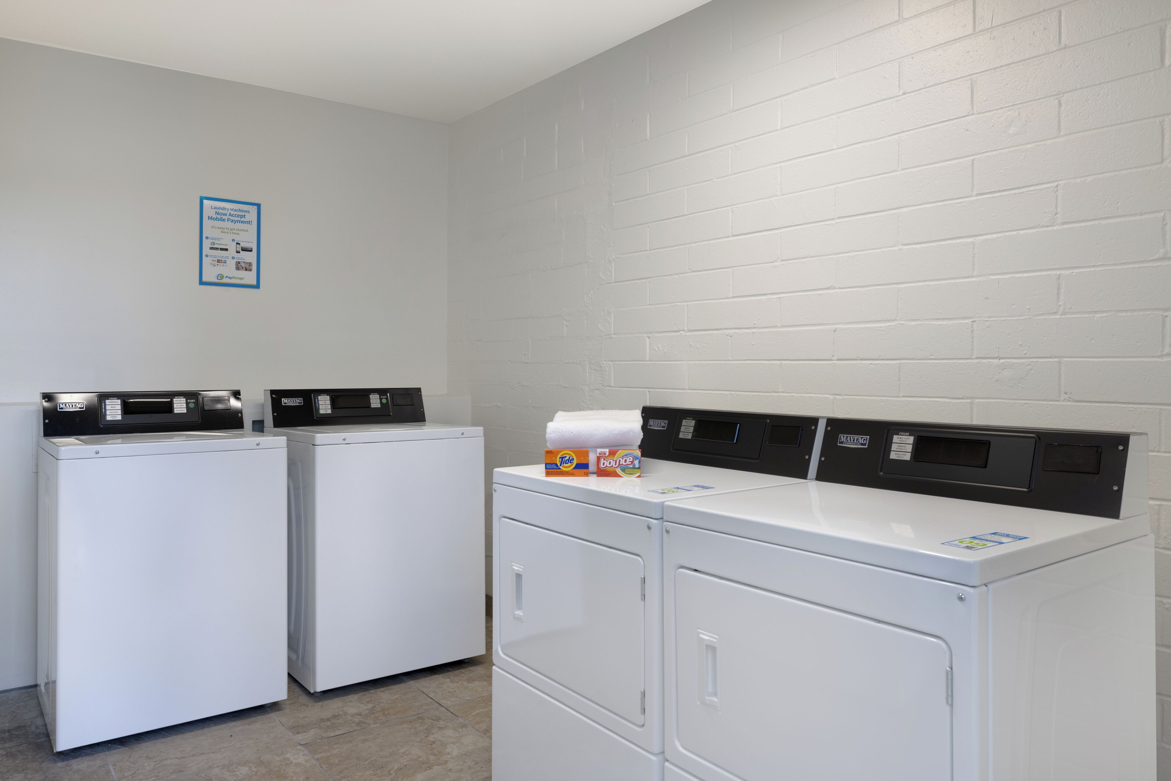 A laundry area with two front-loading washers and a dryer, a white brick wall, and a notice on the wall.