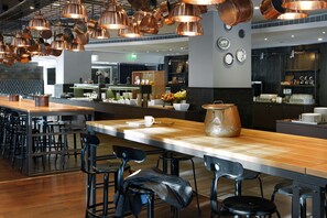 Un restaurante moderno con una barra alargada, varias zonas de estar e iluminación colgante de cobre.