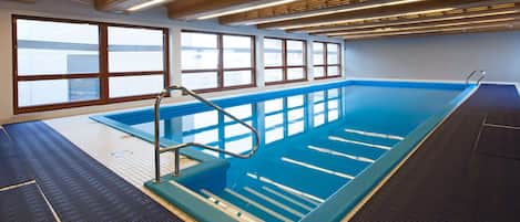 Una piscina con suelo de baldosas, una escalera de metal y amplias ventanas.
