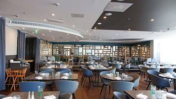 A modern restaurant with a curved ceiling, wooden bookshelves, and a variety of seating options including tables and chairs.