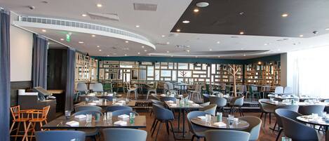 Un ristorante moderno con soffitto curvo, scaffali in legno e diverse opzioni di seduta tra cui tavoli e sedie.