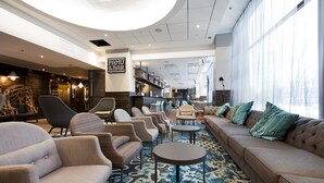 A modern lounge area with sofas, armchairs, and tables, featuring a large window and a sign for 'FAMU & BAR'. - Scandic Park Helsinki (Helsinki)