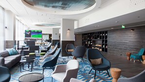 A modern lobby with seating areas, a television displaying sports, and a bar area. - Scandic Park Helsinki (Helsinki)