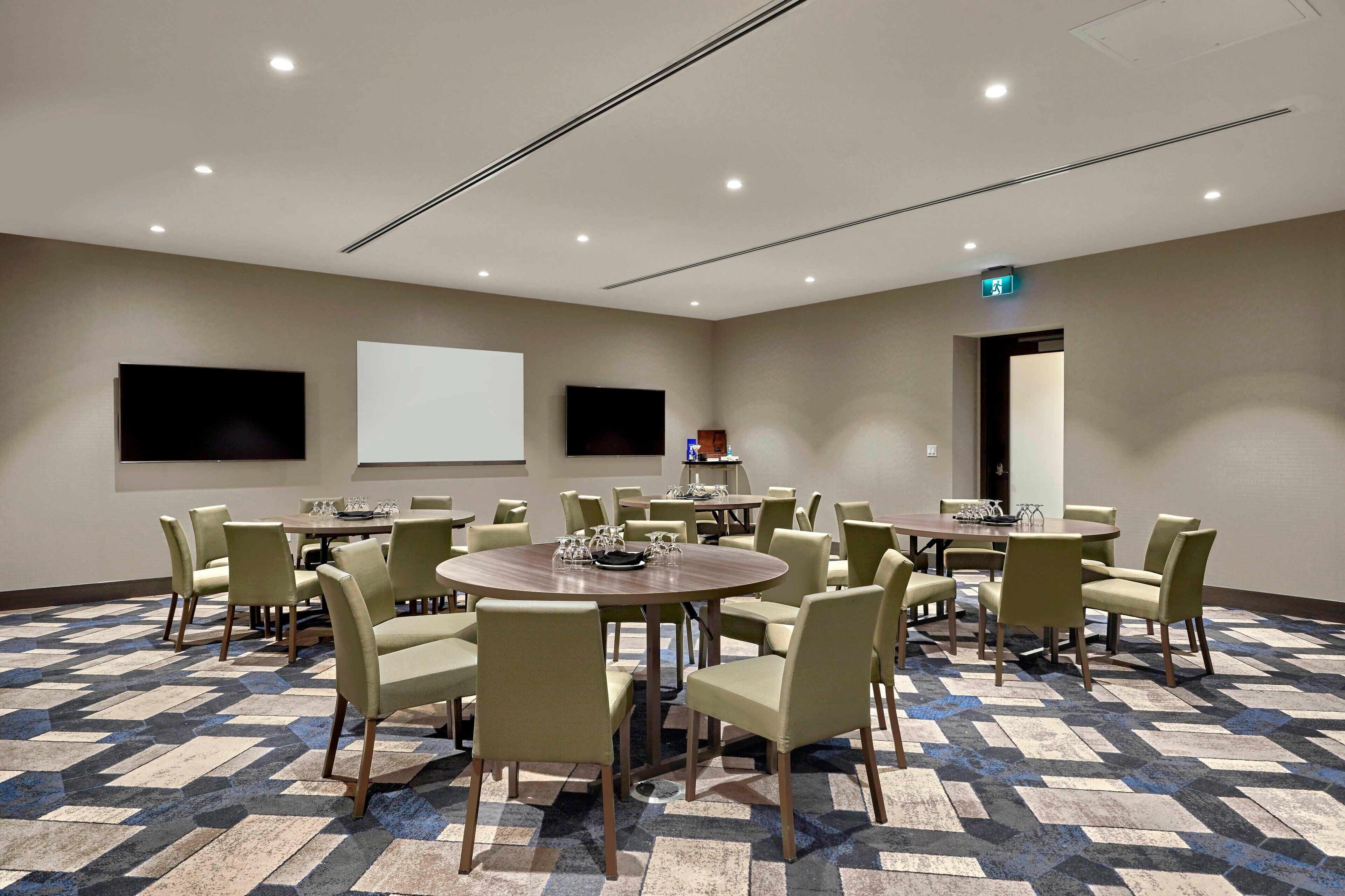 A conference room with multiple tables and chairs, a projector screen, and a carpeted floor.