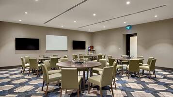 A conference room with multiple tables and chairs, a projector screen, and a carpeted floor.