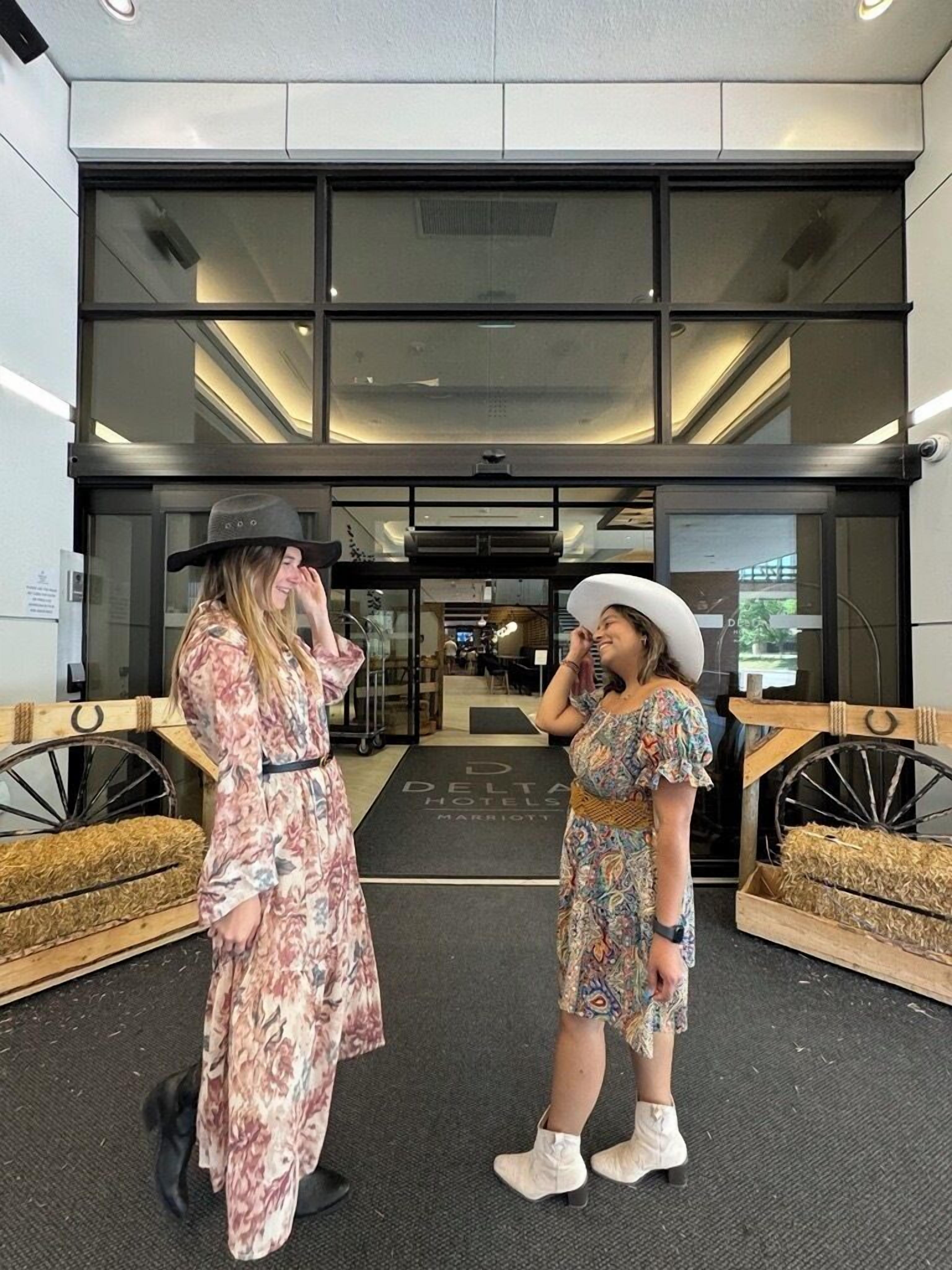 Due donne davanti all'ingresso di un hotel dal design moderno, con ampie vetrate e un interno ben visibile.