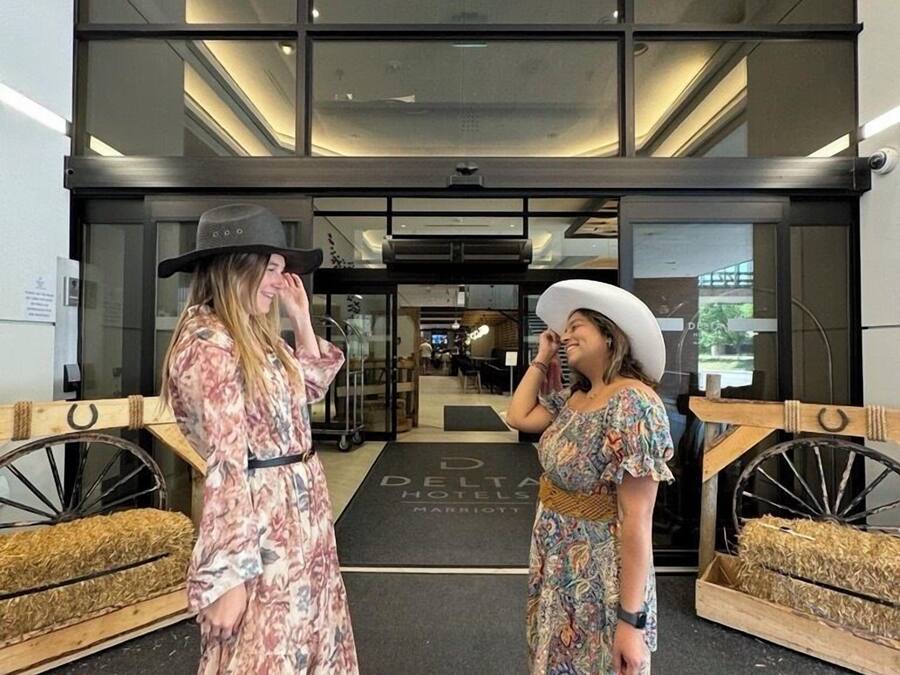 Due donne davanti all'ingresso di un hotel dal design moderno, con ampie vetrate e un interno ben visibile.