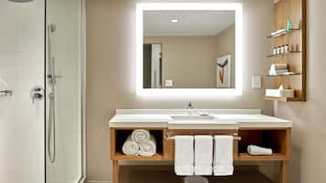 A modern bathroom with a glass shower enclosure, a large mirror, and a vanity with a sink and towel storage.