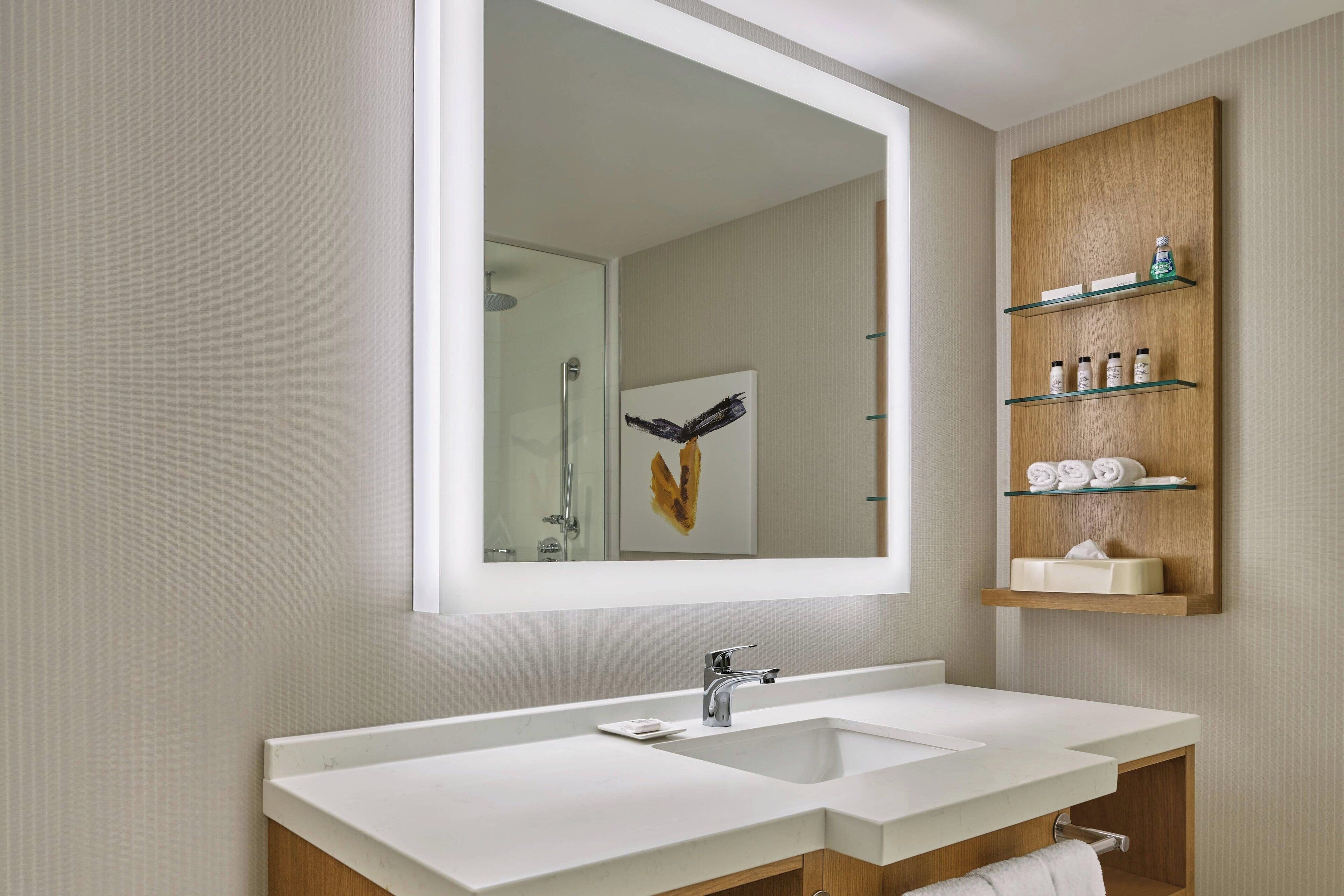 Un baño moderno con un espejo grande, dos lavamanos y estantes de madera con artículos de aseo.