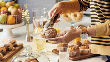 Una persona sirviendo muffins en un mostrador con una variedad de productos horneados y bebidas.