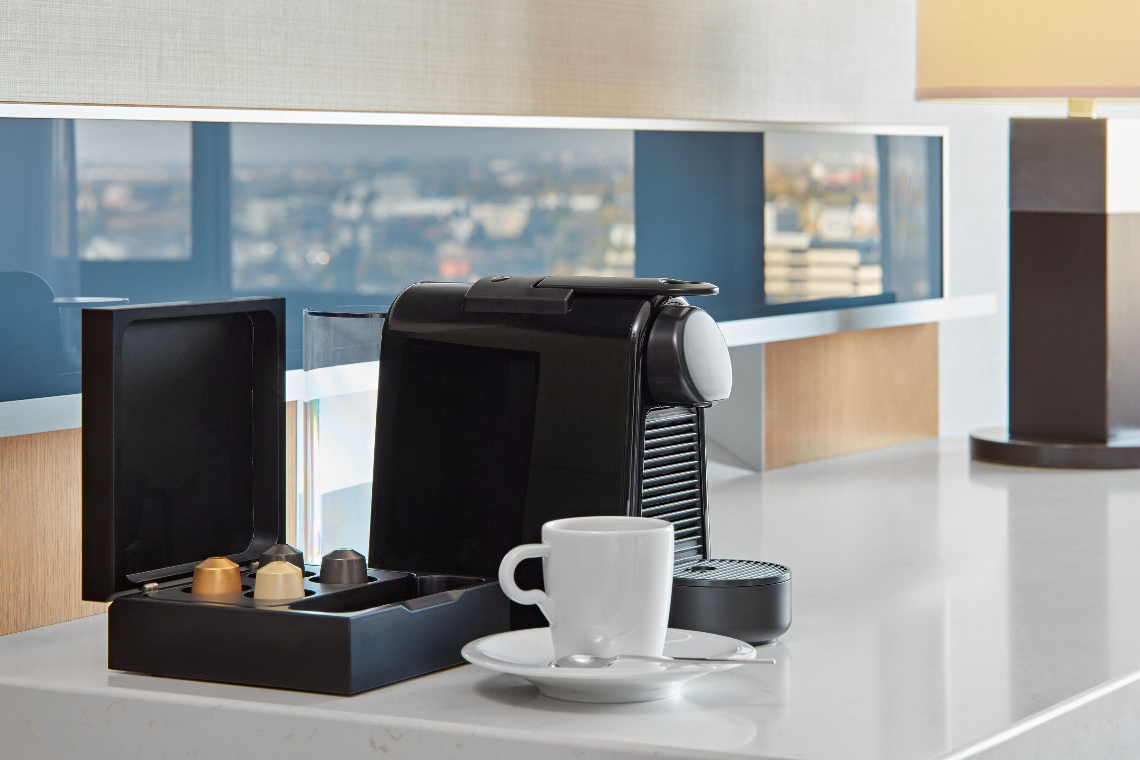 A coffee machine with a cup and saucer on a counter, with a window view in the background.