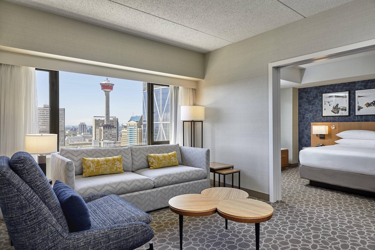 Et hotelværelse med sofa, lænestol og seng. Der er udsigt til byens skyline gennem vinduet.