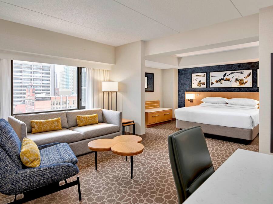 A hotel room with a sofa, two round tables, a bed, and artwork on the wall.