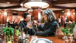 A couple toasting with martinis in a warmly lit, elegantly furnished restaurant with wooden beams and a high ceiling. - Hotel Sorrento (Seattle)