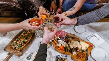 A group of people toasting with drinks around a table with a variety of cheeses, meats, and bread.