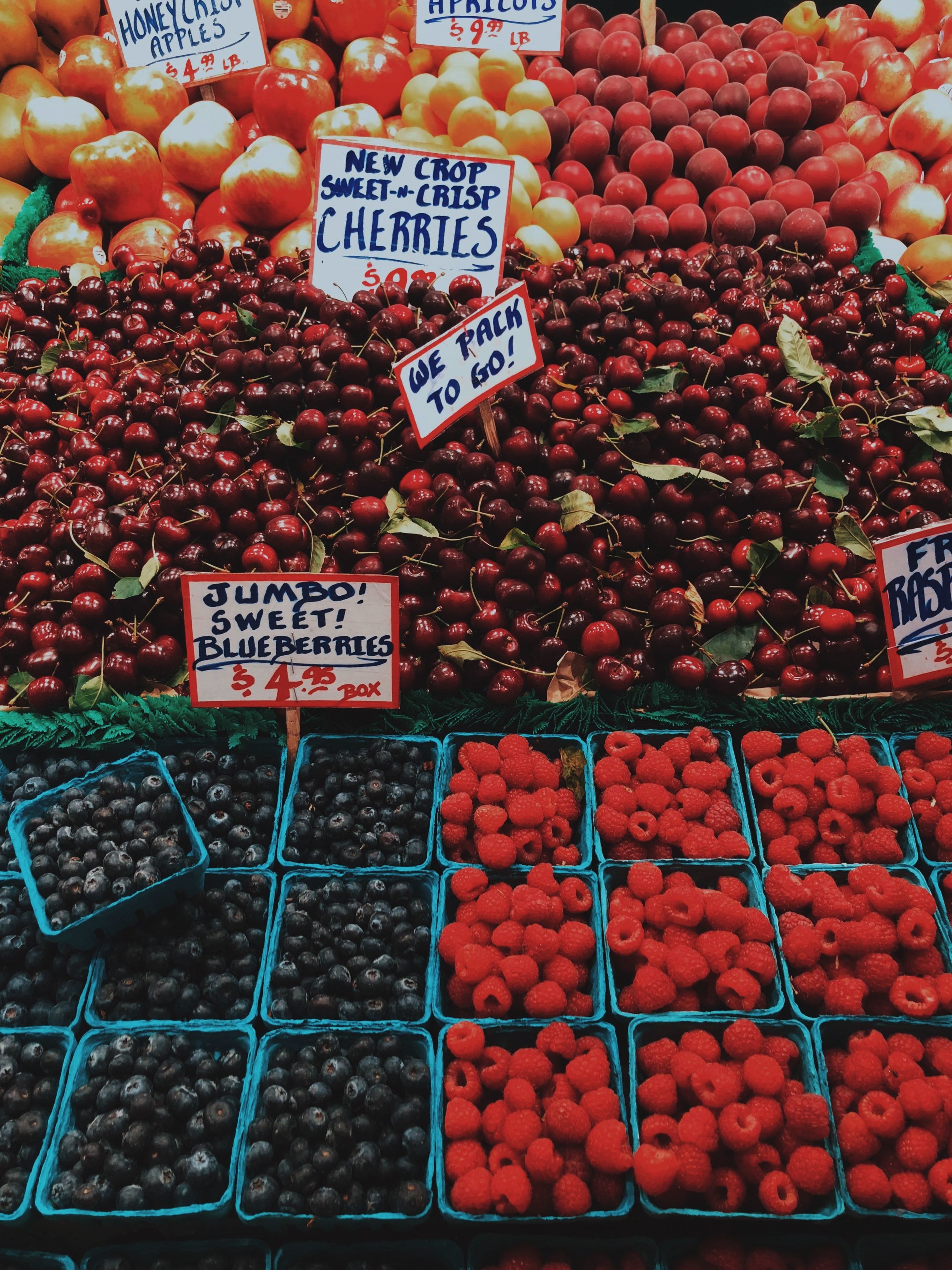 A fruit market with various fruits like apples, cherries, and berries displayed in bins.