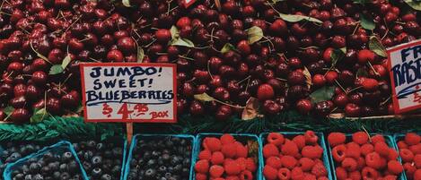 A fruit market with various fruits like apples, cherries, and berries displayed in bins.