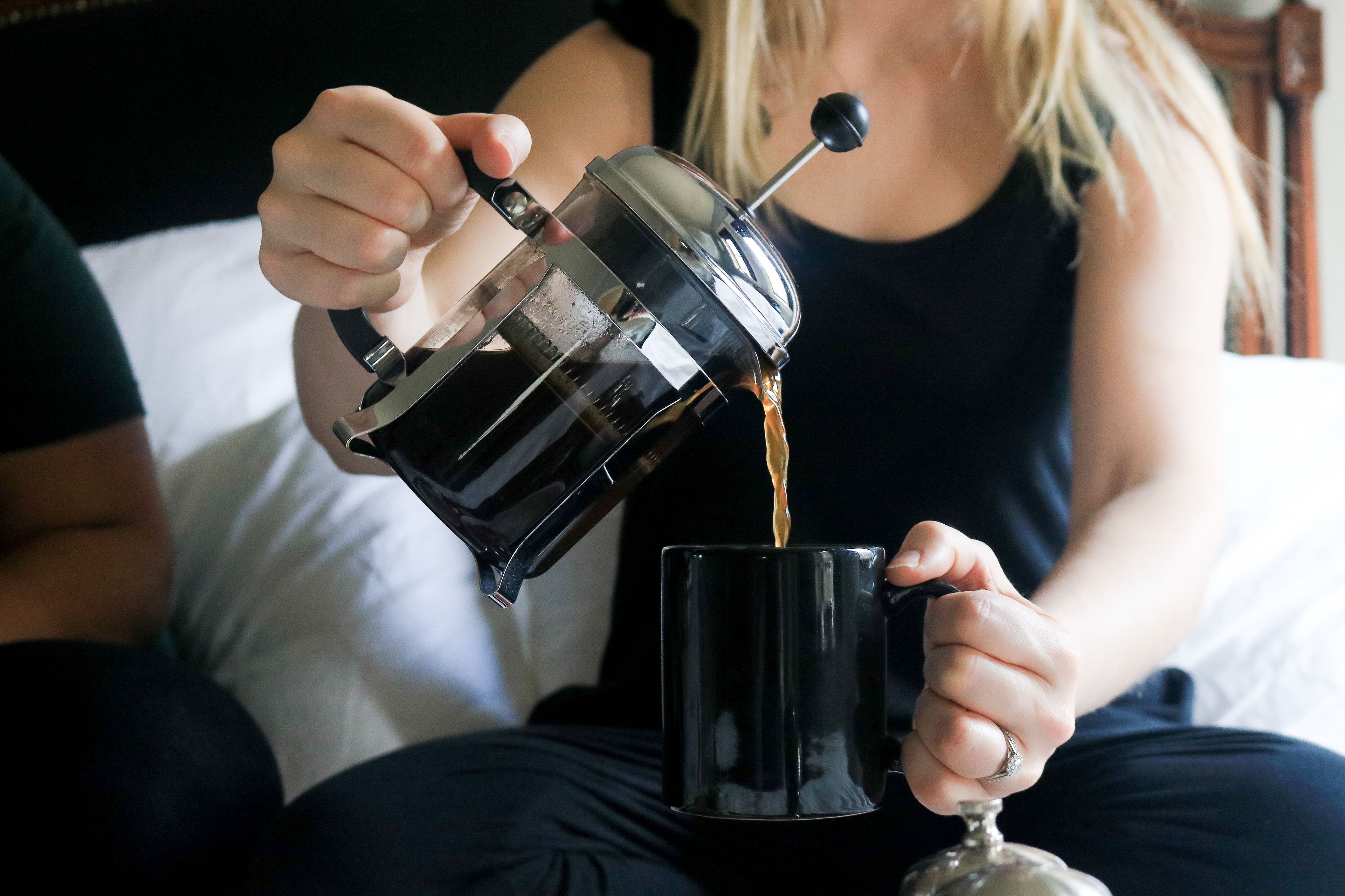 A person pouring coffee from a French press into a black mug.