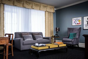A living room with a grey sofa, a matching armchair, a coffee table with books, and a lamp.