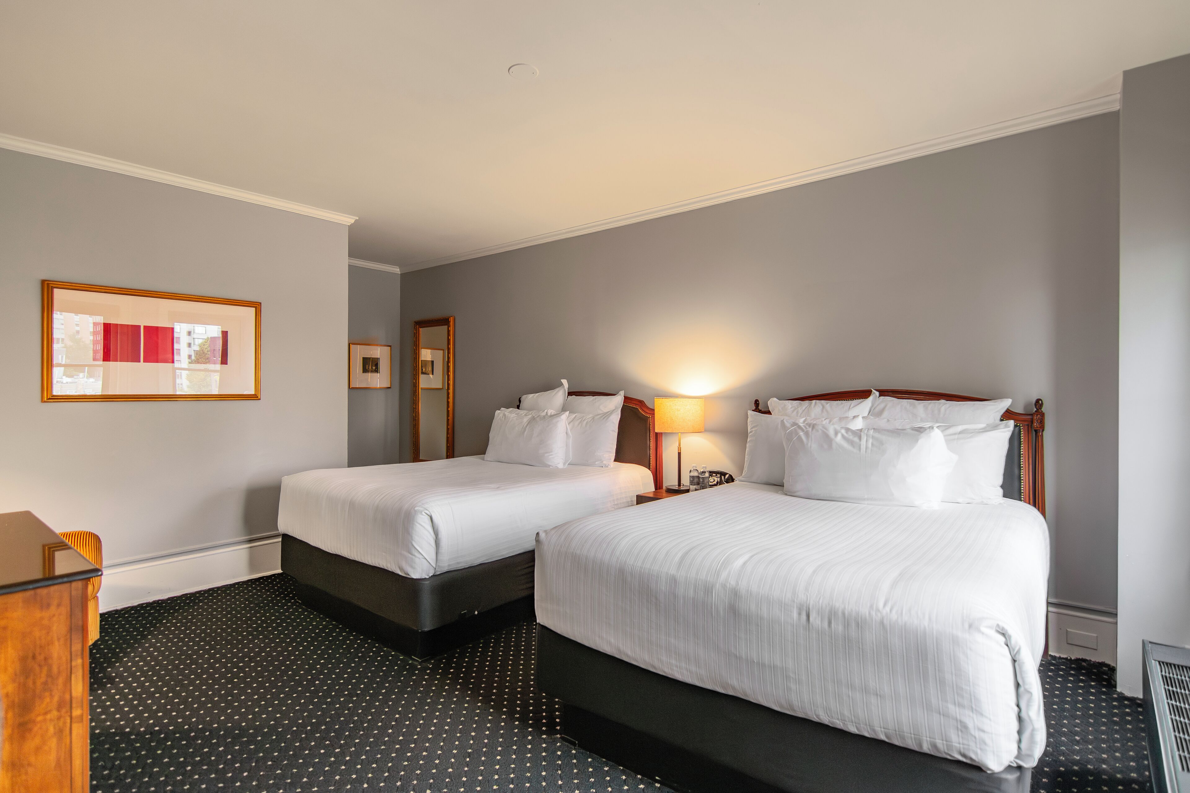 A hotel room with two beds, a desk, and a lamp.