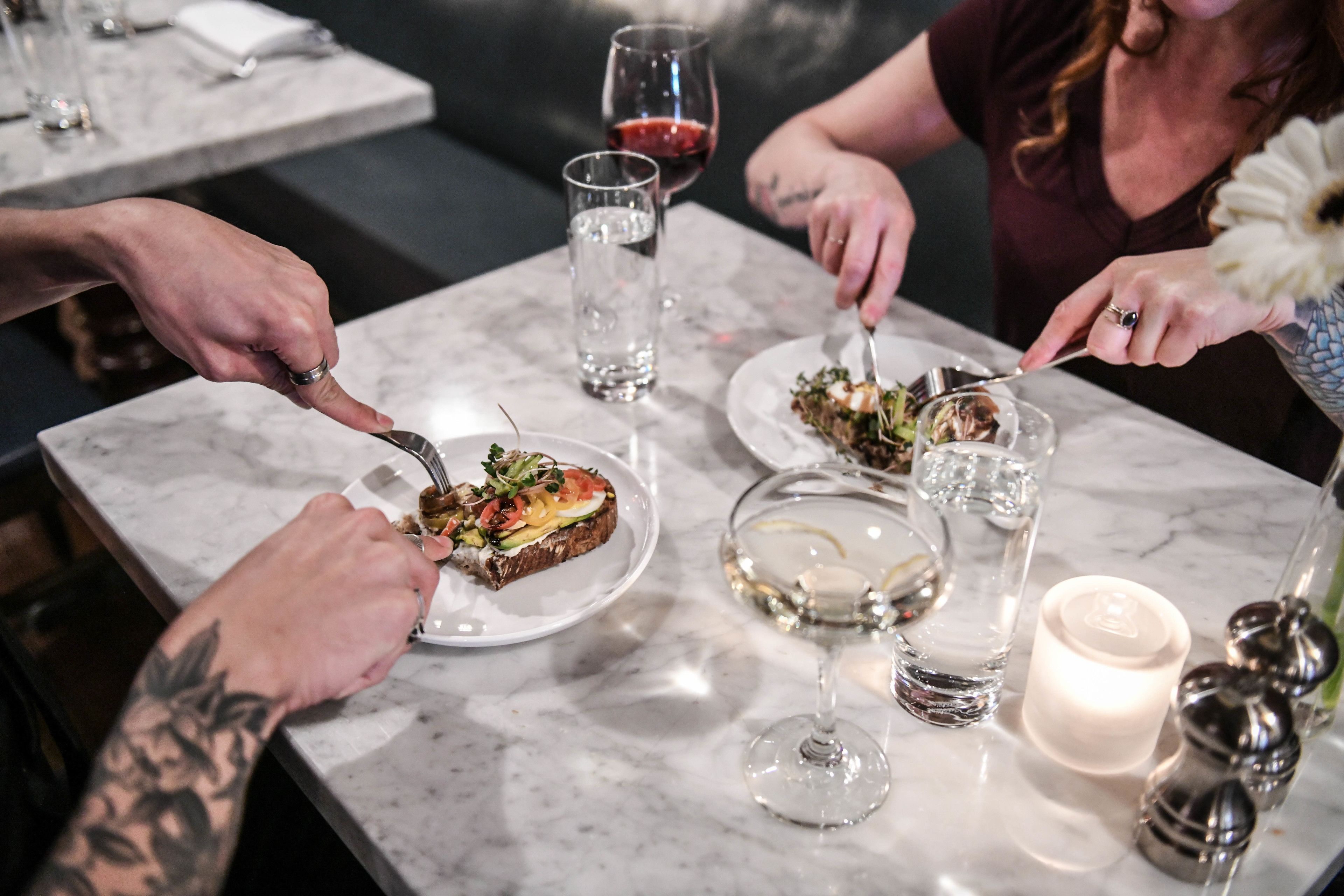 A marble dining table with plates of food, glasses of water and wine, and a candle.