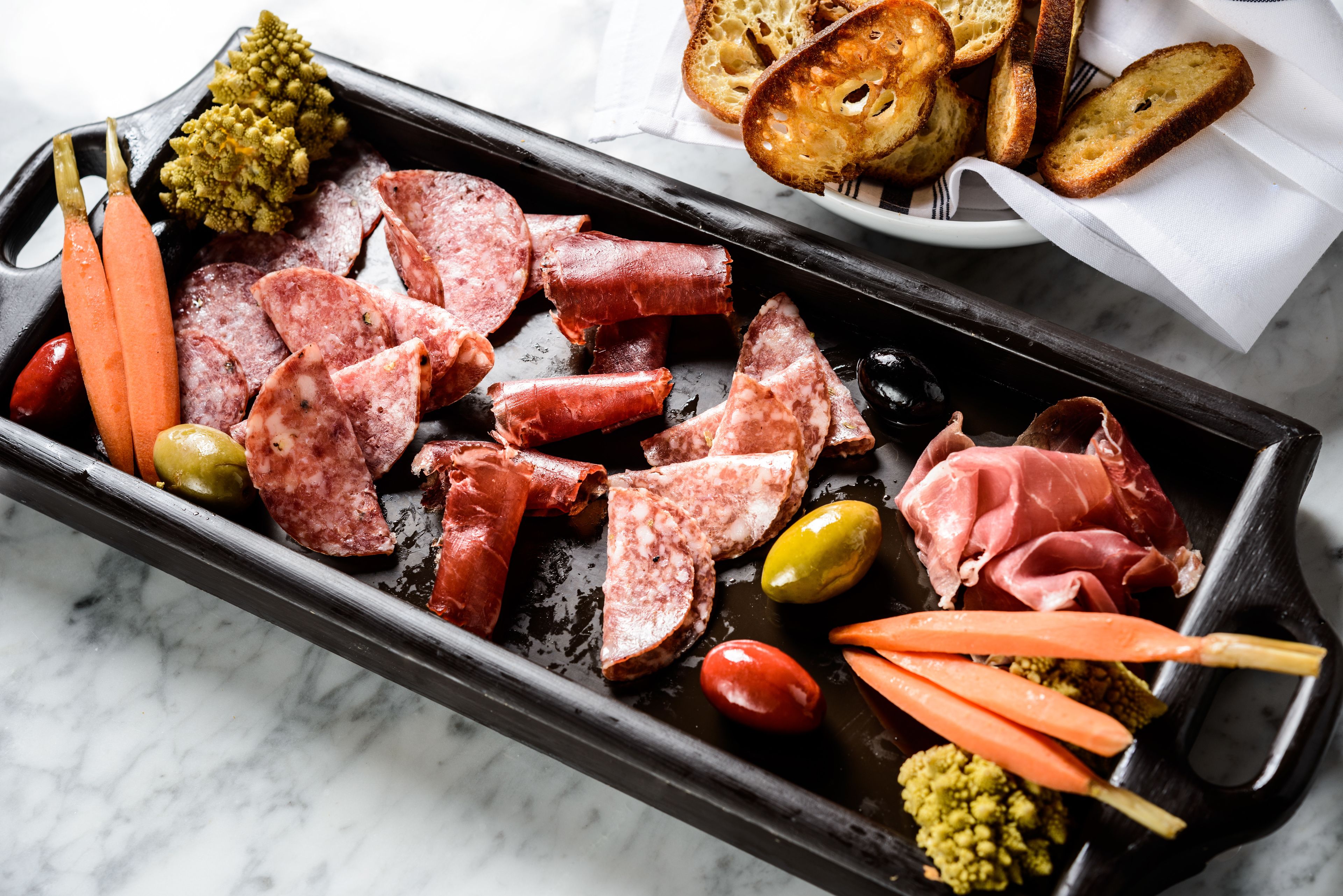 A charcuterie board with various meats, olives, and vegetables.