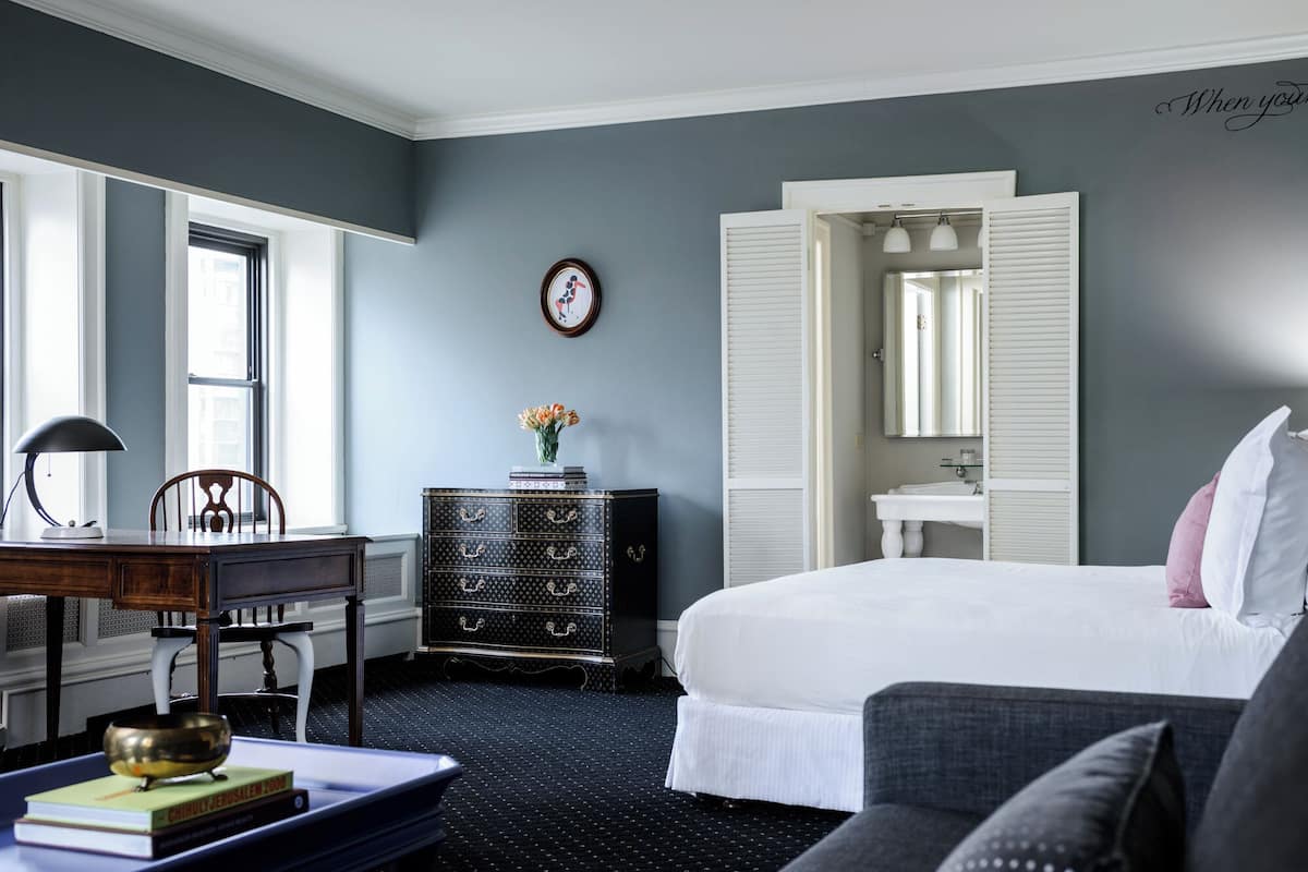 Una habitación de hotel con una cama, un escritorio con lámpara, un aparador y una ventana.