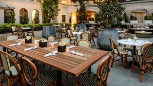 An outdoor dining area with wooden tables and wicker chairs, surrounded by greenery and a brick building in the background. - Hotel Sorrento (Seattle)