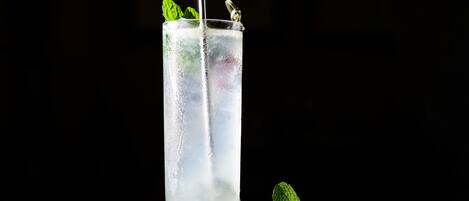 Un grand verre rempli d’une boisson glacée, garni de feuilles de menthe, avec une paille et un élément décoratif en métal, posé sur une surface sombre avec un fond noir.