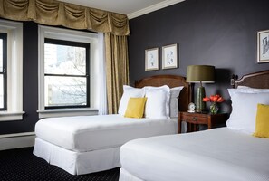 A hotel room with two beds, a nightstand, a lamp, and a window with curtains.
