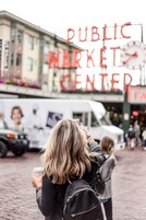 A person holding a cup, standing in front of a sign that reads "PUBLIC MARKET CENTER".