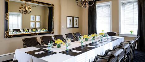 A conference room with a long table, chairs, a chandelier, and a large mirror on the wall.