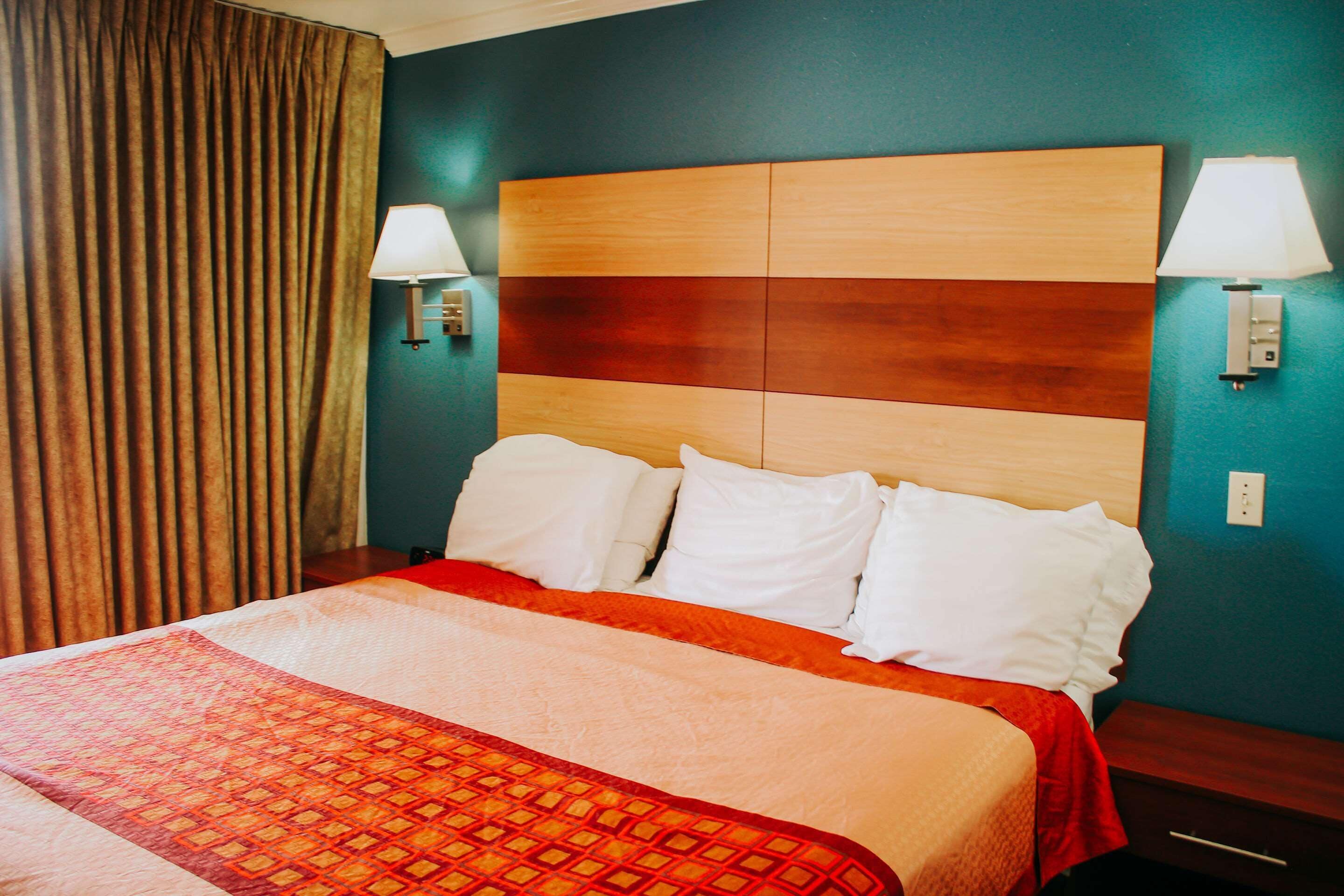 Quarto de hotel com uma cama grande, duas luminárias de cabeceira e uma cabeceira com design de painel de madeira.