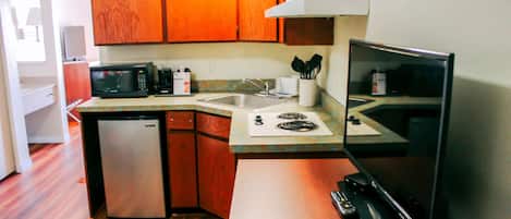Una cocina compacta con armarios de madera, un microondas, un refrigerador pequeño, un lavamanos y una estufa.