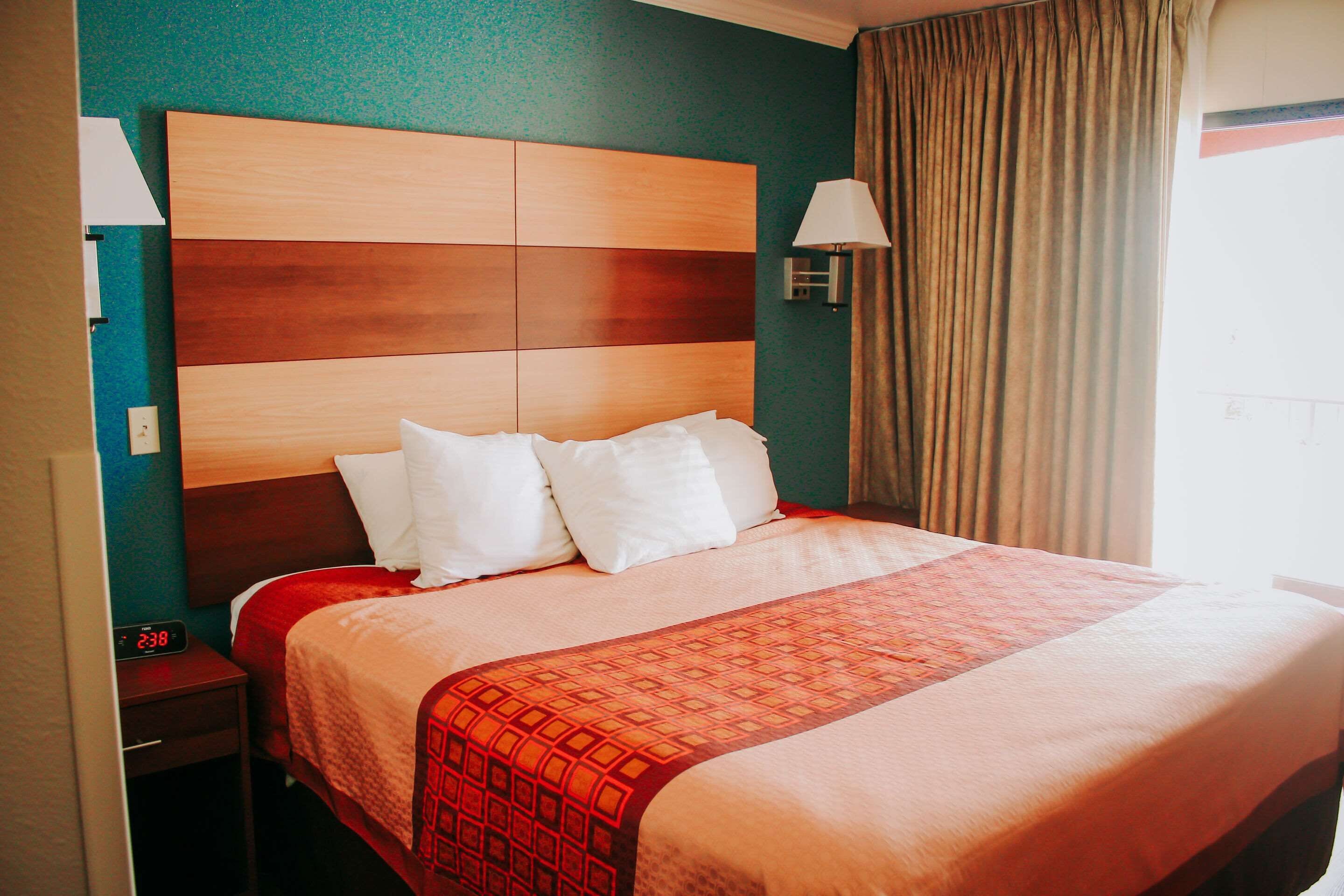 Una habitación de hotel con una cama grande, una mesita de noche con un reloj y una lámpara de pared.