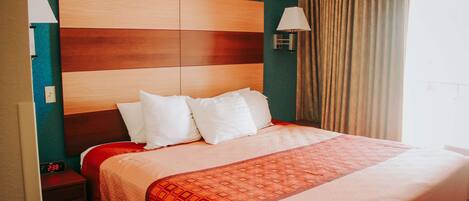 Una habitación de hotel con una cama grande, una mesita de noche con un reloj y una lámpara de pared.